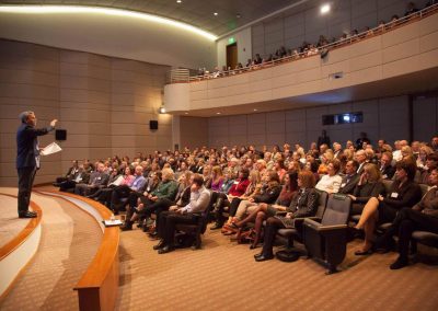 A speaker addresses a large audience in The Cable Center’s Malone Theater, with attendees spanning both main and balcony levels.