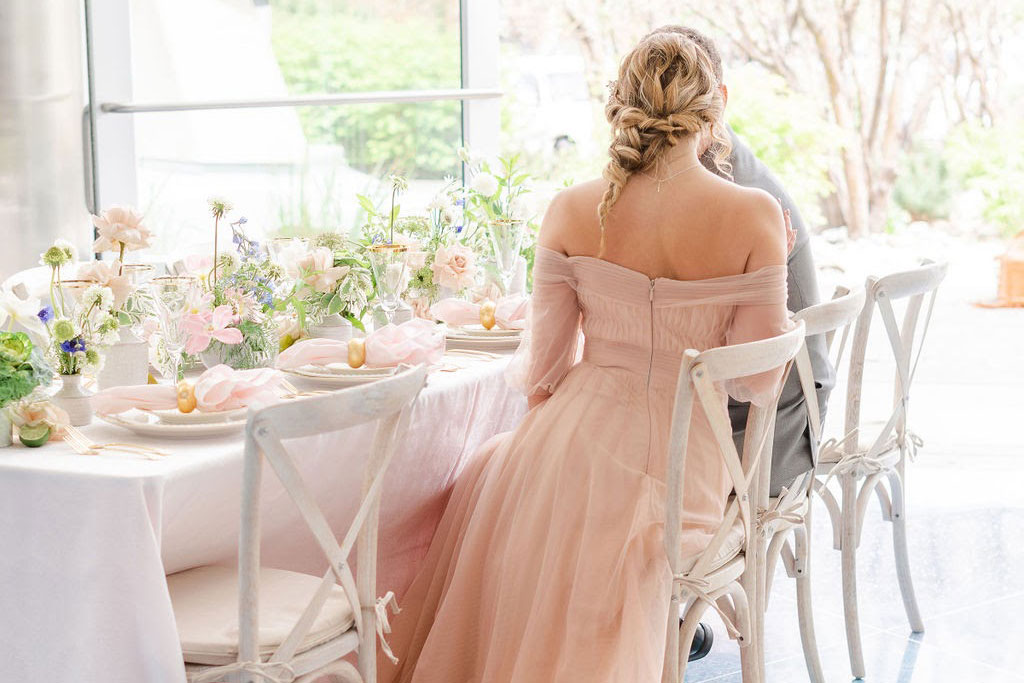 A bride at her wedding sitting at a table in a pink dress.