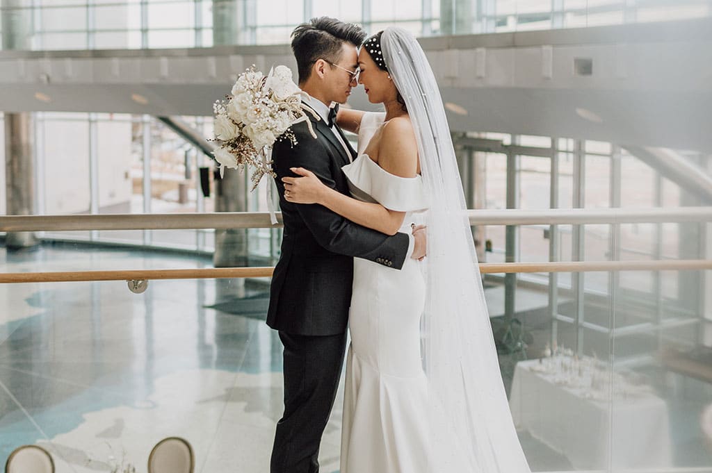A bride and groom embracing and kissing at the Cable Center, the bride holding a large bouquet.