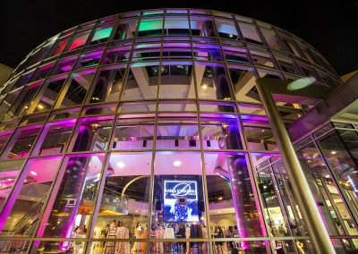 Illuminated modern glass building at night with people inside and a large screen displaying text. The Cable Center is an elegant event venue perfect for any occasion.