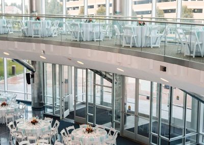 The Cable Center, a spacious, perfectly elegant Denver event venue with large floor-to-ceiling windows, set up with round tables covered in white tablecloths and arranged for an event. The upper level has additional tables and chairs, creating a completely unique setting.