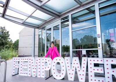 A woman in a bright pink outfit stands outside The Cable Center’s glass entrance, behind large illuminated letters spelling "FEMPOWER," creating an elegant scene at this unique Denver event venue.