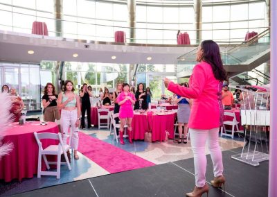A woman in a bright pink blazer speaks to an audience standing beside unique pink table settings at at The Cable Center, an elegant Denver event venue.