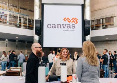 People stand and chat in front of a large screen displaying the Canvas Credit Union logo at an elegant indoor event hosted at The Cable Center event venue in Denver.
