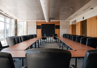 Bresnan Board Room with an elegant U-shaped wooden table, comfortable black leather high-back chairs, large windows on the left, and a black screen on the wall at the front. This space is perfect for meetings or gatherings at The Cable Center, a premier Denver event venue.