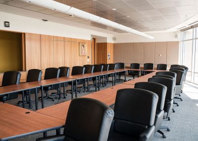 The Cable Center’s modern Bresnan Board Room with a U-shaped arrangement of tables and black leather chairs, wood-paneled walls, carpeted flooring, and a large window allowing natural light to enter.