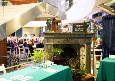 A decorative fireplace, adorned with a "Welcome to the Teller House, Please Come In" sign, graces the reception area of The Cable Center event venue in Denver. People are seated at tables in the background, under modern architectural elements.
