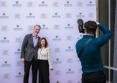 Two people pose elegantly for a photo on a step and repeat backdrop with logos for "Greenhouse Scholars" and "Glass Half Full." A photographer captures their unique image at The Center Center event venue in Denver.