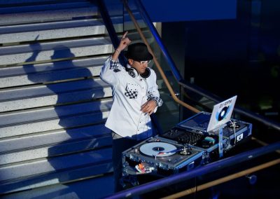 A DJ wearing a hat and headphones is performing on a staircase with turntables and a laptop at The Cable Center, an elegant Denver event venue.