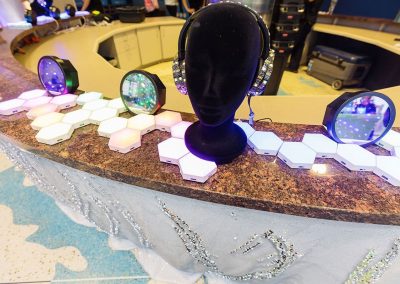 A unique display featuring a black mannequin head with headphones, hexagonal light panels with multicolored lights, and circular LED mirrors elegantly arranged on a marble countertop.