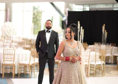 A woman in an ornate dress stands in the foreground while a man in a suit stands behind her in the large, elegant Daniels Great Hall at The Cable Center in Denver, with tables and chairs set up for a unique wedding.