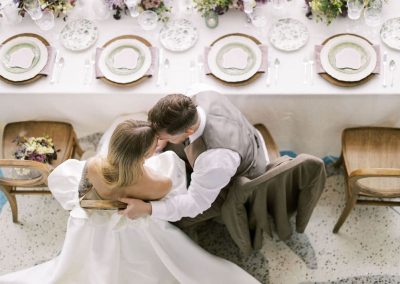 A wedding couple, viewed from above, sits closely with foreheads touching at a decorated table set for a formal event at The Cable Center, an elegant Denver event venue.