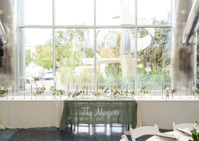 An elegant long table, adorned with candles and flowers, is set in front of large windows with a green banner that reads “The Nguyens.”