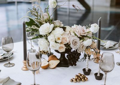 Elegantly set dining table with white and grey linens, floral centerpiece with white and cream flowers, candle holders with lit candles, wine glasses, and place settings for four at The Cable Center, a unique Denver event venue.
